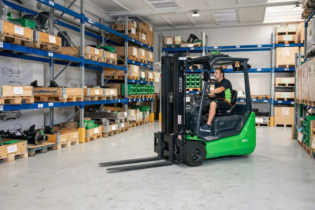 Bestuurder op een groene CESAB B3-20 heftruck rijdend door een magazijn met blauwe stellingkasten. — Prins Maasdijk