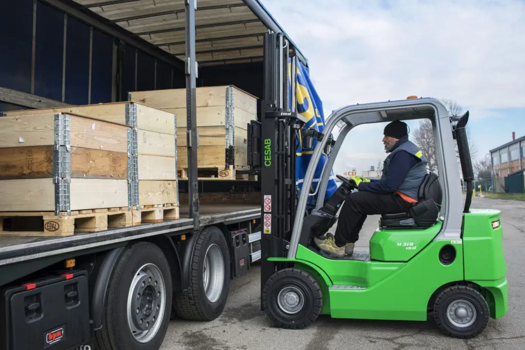 Bestuurder op een groene CESAB M318 heftruck die houten kisten laadt op een vrachtwagen. — Prins Maasdijk