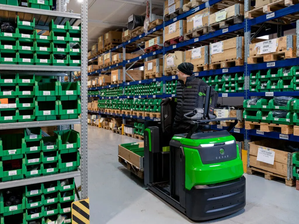 Magazijnmedewerker transporteert pallet met CESAB O1 elektrische palletwagen in smal gangpad van onderdelen magazijn | Prins Maasdijk