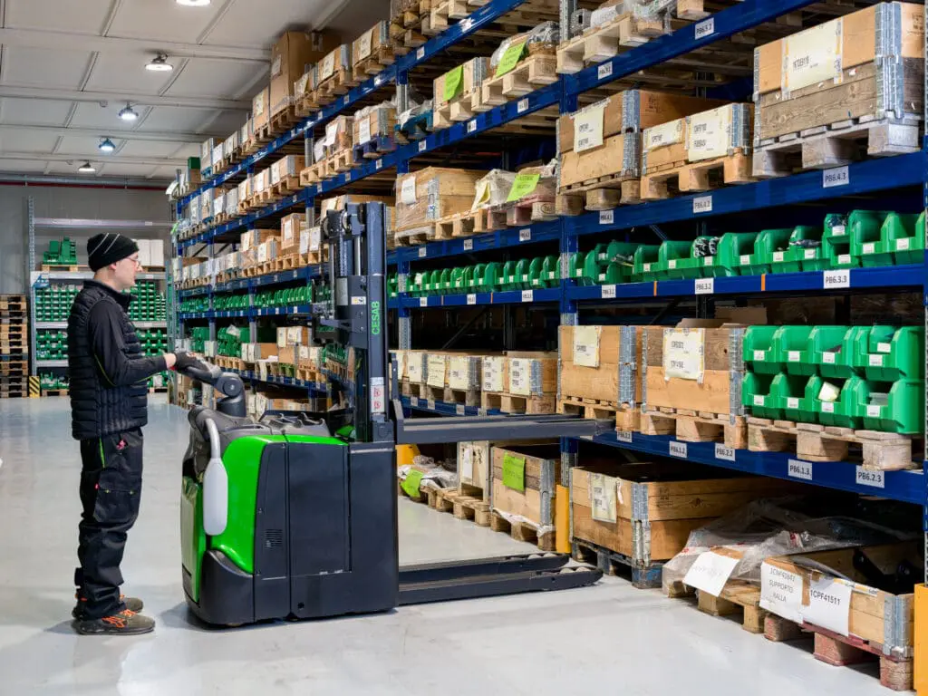 Magazijnmedewerker bedient CESAB S320DN elektrische stapelaar bij stellingen in onderdelen magazijn | Prins Maasdijk