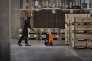 Magazijnmedewerker bedient Toyota BT Tyro elektrische palletwagen tussen pallets met houten kisten in magazijn | Prins Maasdijk