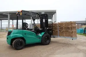 Groene Prins Bulldog 25-E elektrische heftruck met een stapel houten pallets op een buitenterrein, linker zijaanzicht. — Prins Maasdijk
