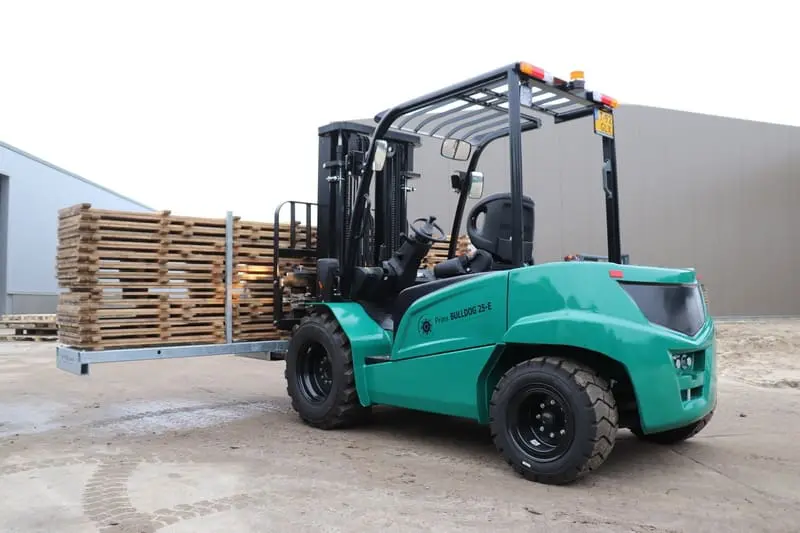 Groene Prins Bulldog 25-E elektrische heftruck met een lading houten pallets buiten bij een bedrijfshal, rechter zijaanzicht. — Prins Maasdijk