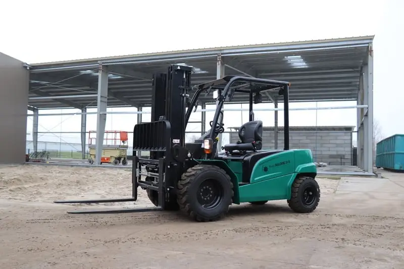Groene Prins Bulldog 25-E elektrische heftruck buiten op een zandterrein naast een bedrijfshal, vooraanzicht. — Prins Maasdijk