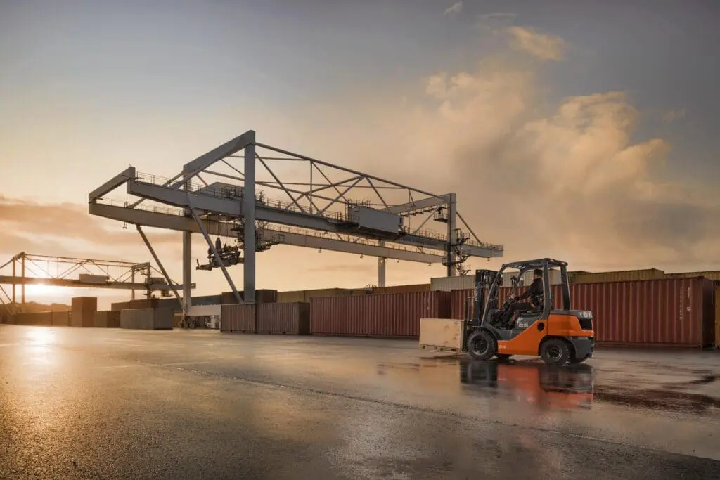 Magazijnmedewerker rijdt met Toyota Tonero LPG heftruck op containerterminal bij havenkranen tijdens zonsondergang | Prins Maasdijk