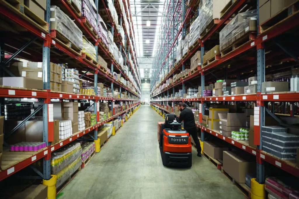 Magazijnmedewerker pickt orders met Toyota BT Optio OSE250 elektrische orderpicker in lang gangpad van groot distributiecentrum | Prins Maasdijk