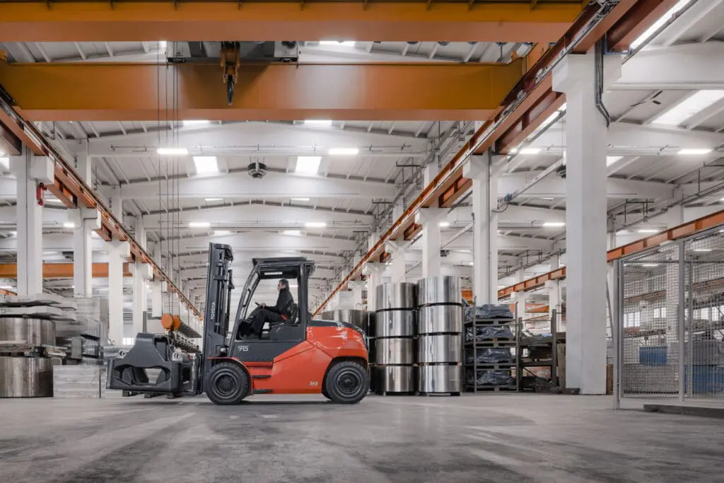 Toyota Traigo 80 elektrische heftruck met clampattachment verplaatst stalen rollen in industriële productiehal | Prins Maasdijk