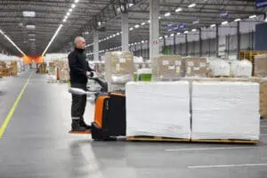 Magazijnmedewerker rijdt met Toyota BT Levio LPE200B elektrische palletwagen met rijplatform in groot distributiecentrum | Prins Maasdijk
