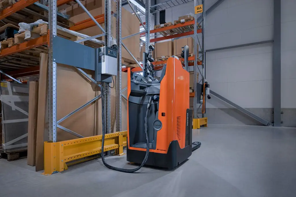 Toyota BT Levio LSI200 elektrische palletwagen aangesloten op lader naast magazijnstelling | Prins Maasdijk